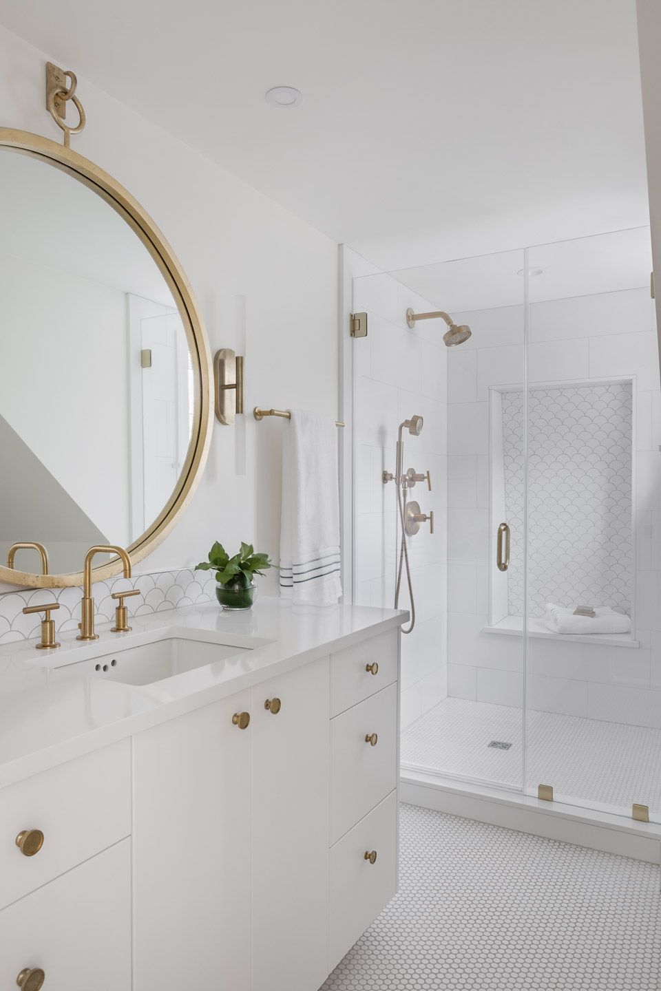 White full bathroom with large circular brass mirror